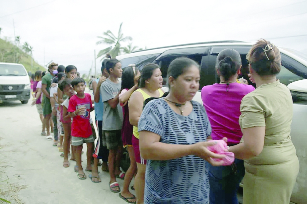 Residents stand in a queue to receive food given by travellers along a highway in Surigao city, Surigao del Norte province on Wednesday, days after Super Typhoon Rai devastated the province. - AFP