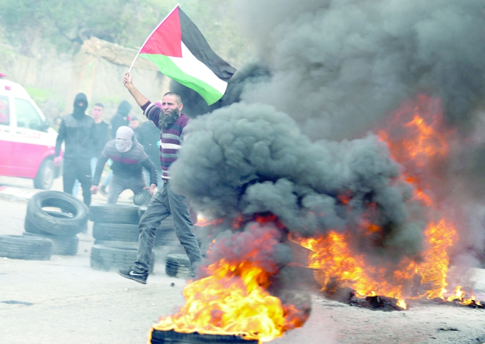 A demonstrator carries a Palestinian flag next to a burning barricade during a protest against Jewish settlements, in Burqa village, in the Israeli-occupied West Bank on Thursday. - Reuters
