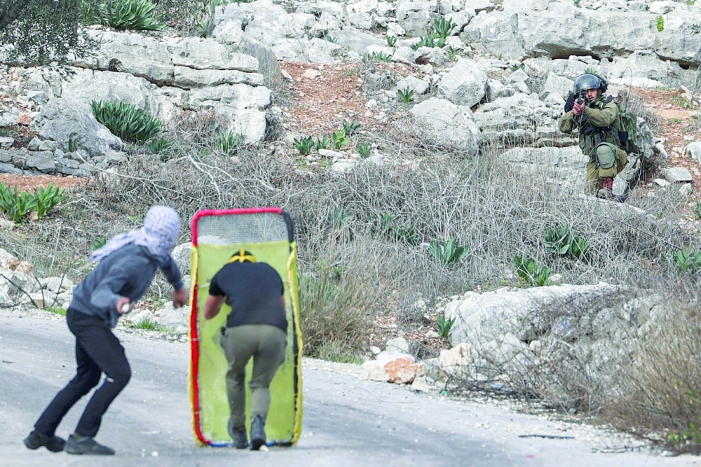 Palestinian protesters take cover during clashes with Israeli security forces following a demonstration against the expropriation of land by Israel, in the village of Kfar Qaddum near the Jewish settlement of Kedumim in the occupied West Bank on Friday. - AFP