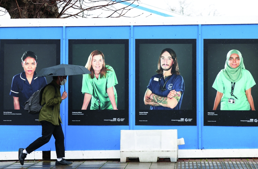 A person walks past images of National Health Service (NHS) workers displayed on hoardings outside a temporary field hospital at St George's Hospital in London. -- Reuters
