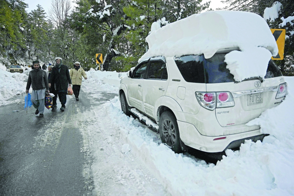 People walk past a vehicle stuck on a road after a blizzard led to visitors being trapped in vehicles along the roads to the resort hill town of Murree, some 70 Kms northeast of Islamabad. - AFP
