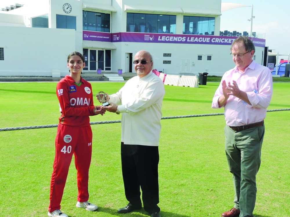Fiza Javed of Oman Women receiving player of the match prize from OC Board Treasurer Kiran Asher as OC Board Member Paul Sheridan claps on.