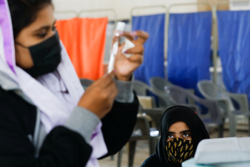 A girl waits as a healthcare worker prepares a dose of coronavirus disease (COVID-19) vaccine to administer at a vaccination centre in Karachi, Pakistan, January 21, 2022. REUTERS/Akhtar Soomro
