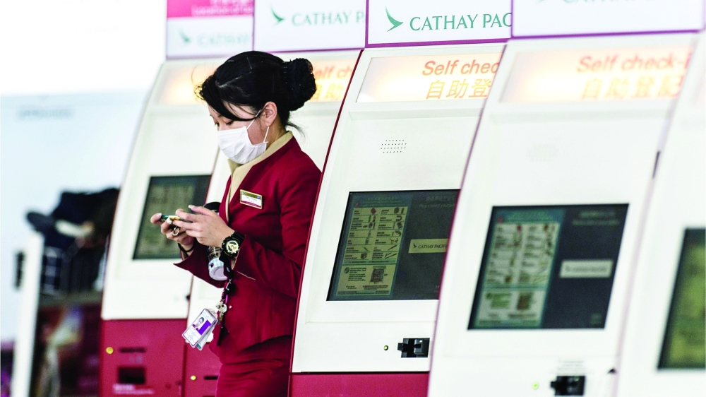 An employee checks her phone at the Cathay Pacific check-in counter in Hong Kong International Airport. — AFP