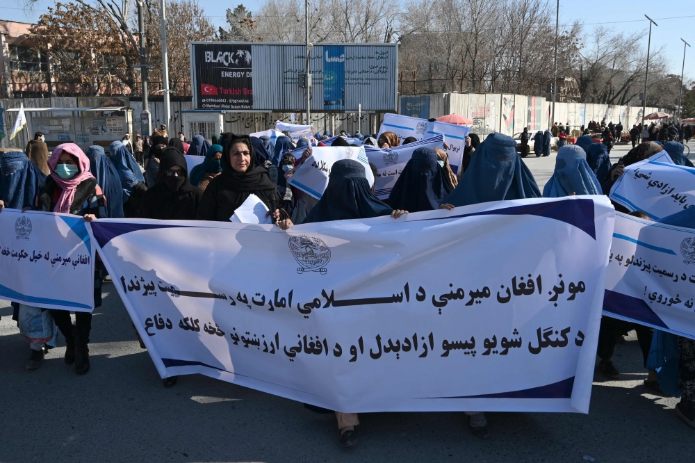 Burqa-clad women hold banners during a women protest in support of the Taliban in front of the US embassy in Kabul on January 26, 2022. 
