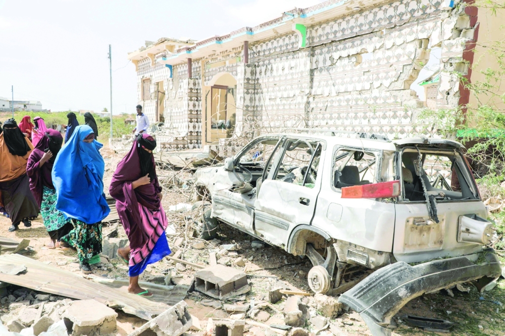 Women walk next to the wreckage of a car following an explosion provoked by Al Shabaab fighters during an attack on the outskirts of Mogadishu. - AFP