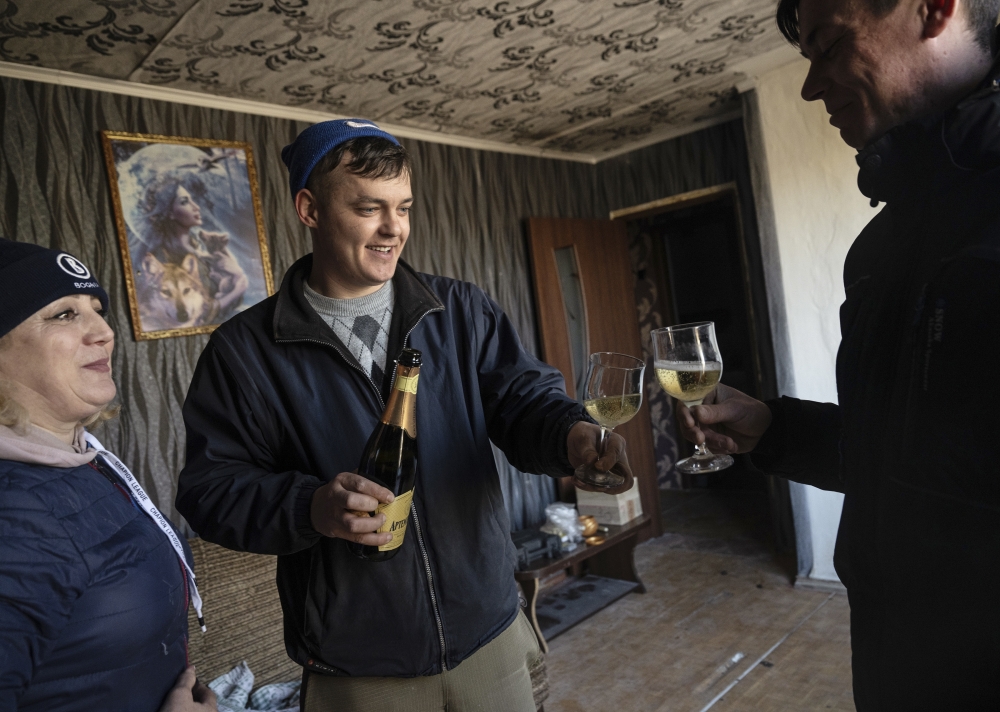 Iryna Yarmulenko, left, toasts with Vladimir Raspatov, center, to celebrate surviving morning shelling in the village of Vrubivka, Ukraine, Feb. 21, 2022. (Lynsey Addario/The New York Times)