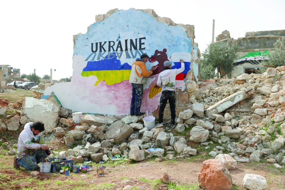 Syrian artists Aziz Asmar and Anis Hamdoun paint a mural amid the destruction, depicting the colours of the Russian and Ukraian flags, to protest against Russia's military operation in Ukraine, in the rebel-held town of Binnish in Syria's northwestern Idlib province on Thursday. - AFP