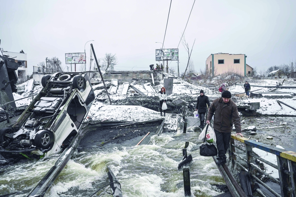 Civilians cross a river on a blown up bridge on Kyiv northern front. - AFP 