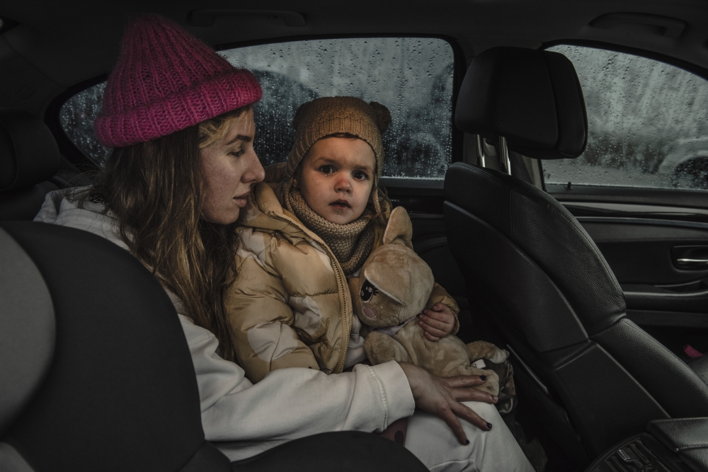 Holding her daughter, a mother from Odessa rests after being picked up by her husband at a border crossing and temporary refugee camp in Palanca, Moldova, March 1, 2022. (Laetitia Vancon/The New York Times)
