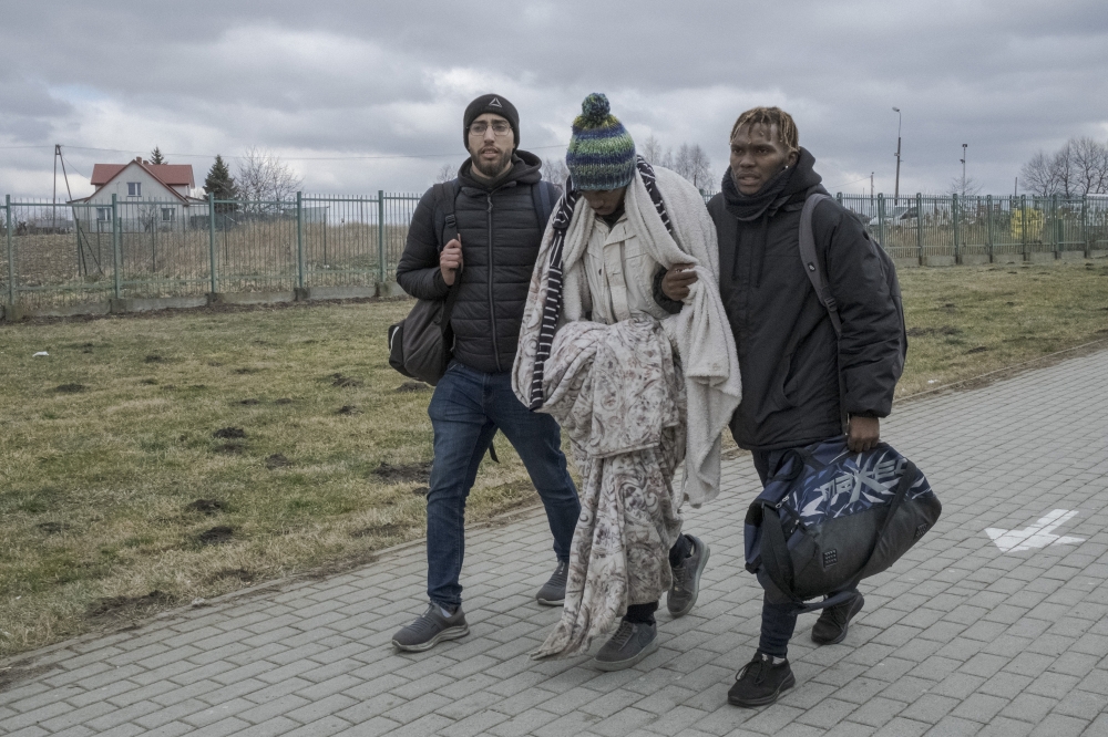 Martin Mpofu, center, a student from Zimbabwe in weak health, is helped by his brother Maneedi, right, and Hatim Redouani, from Morocco, as they cross from Ukraine into  in Medyka, Poland, Feb. 28, 2022.  (Mauricio Lima/The New York Times)