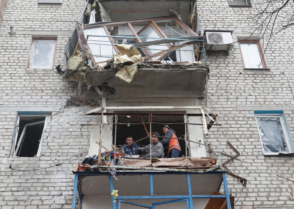 People remove debris from a damaged apartment building in Yasynuvata