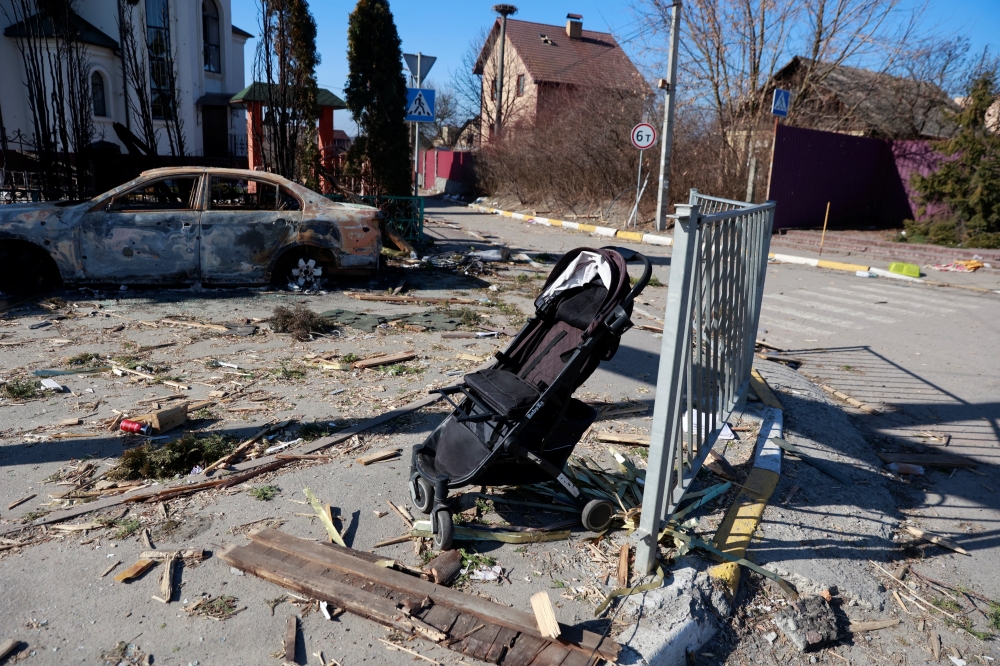A baby pram is seen next to a destroyed car outside of Kyiv
