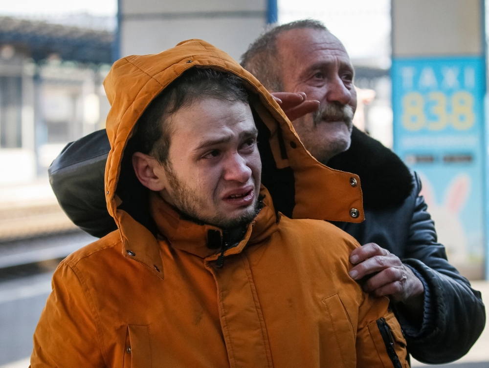 Men react as an evacuation train with their relatives departs to Lviv, at Kyiv central train station in Kyiv