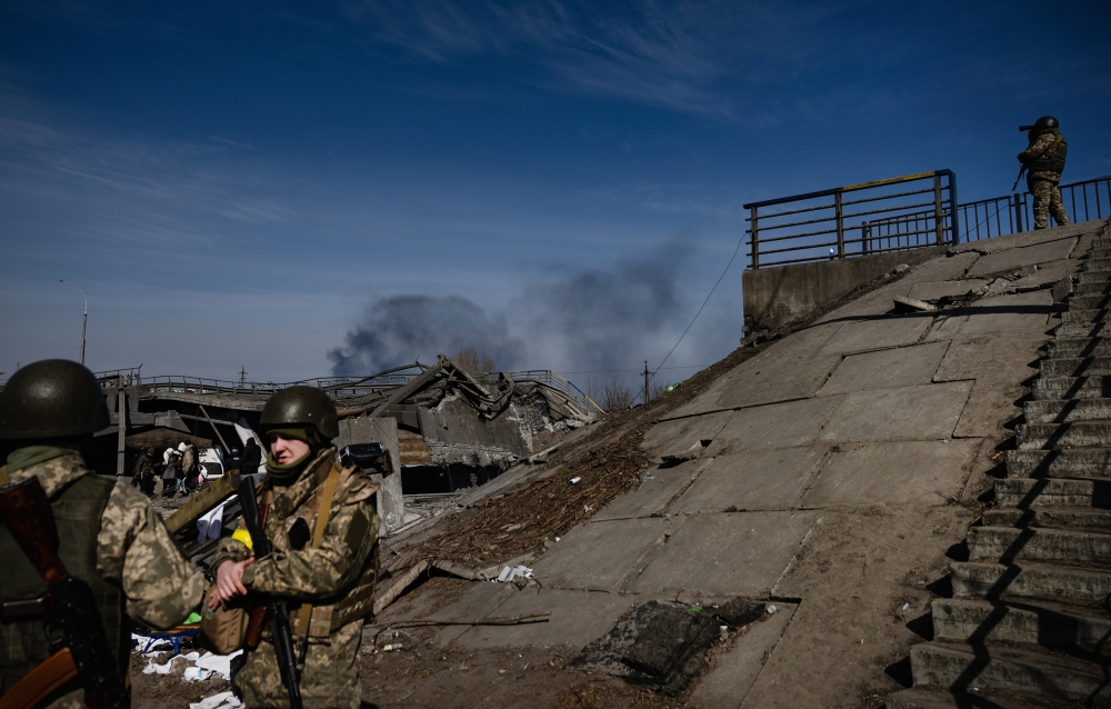 Ukrainian soldiers stand guard at a bridge in the villages of Irpin and Bucha, northwest of Kyiv, fled with the sounds of heavy fighting in the distance on Saturday, March 12, 2022. (Lynsey Addario/The New York Times)