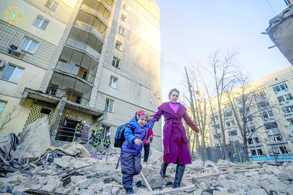 A woman with a child evacuates from a residential building damaged by shelling in Kyiv. -- Reuters