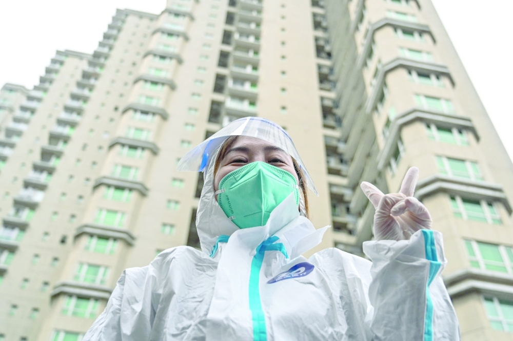 A worker wearing protective gear gestures as people wait to be tested for the Covid-19 coronavirus at a residential compound in Shanghai on Friday. -- AFP

