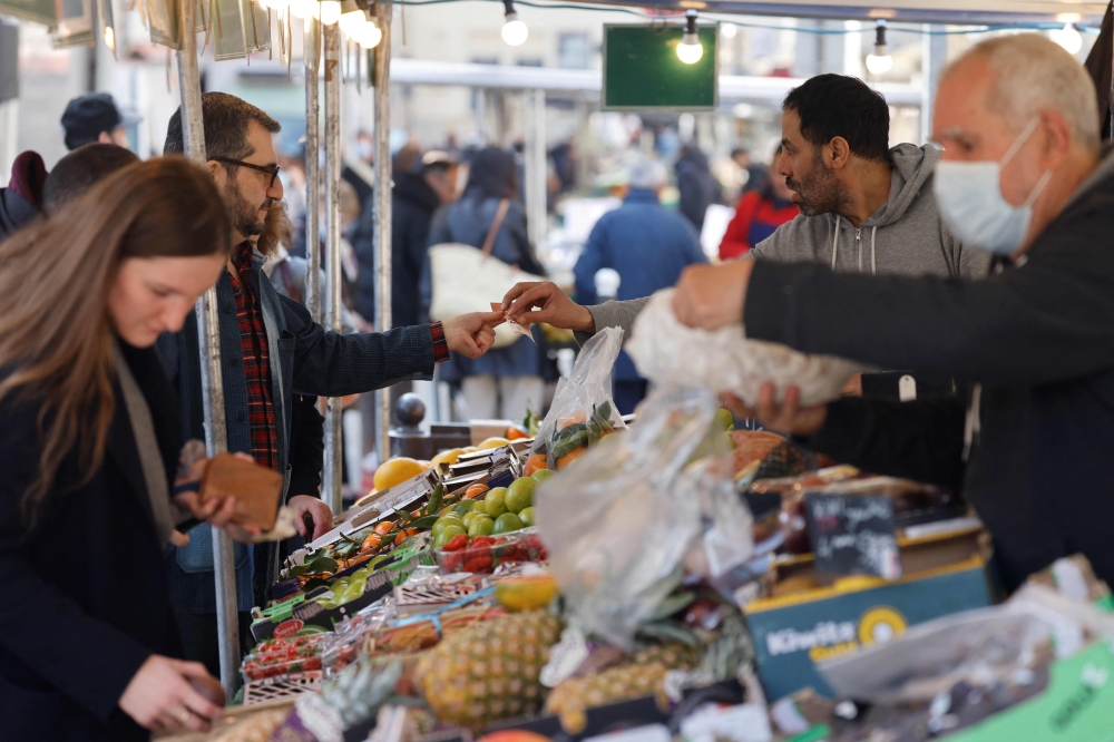Customers buy vegetables at an outside food market place d'Aligre in Paris