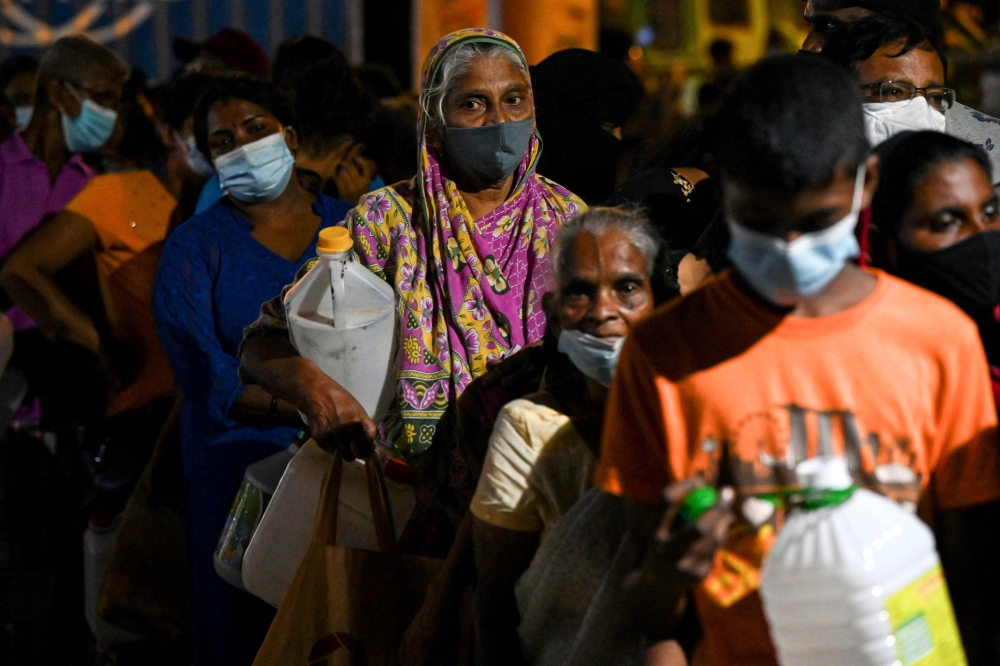 People stand in a queue to buy kerosene oil for home use at a petrol station in Colombo 