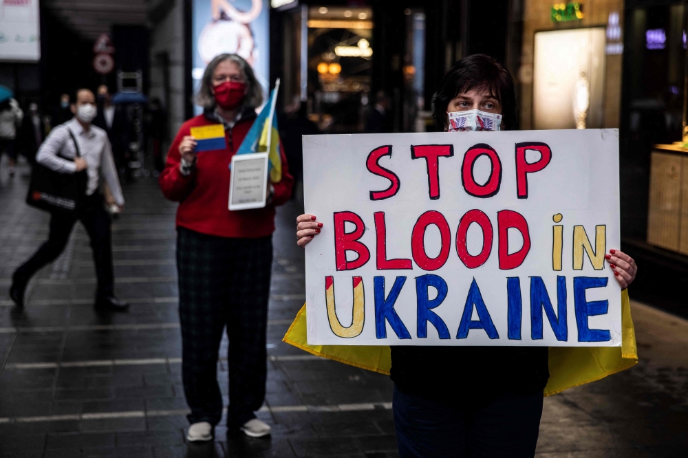 A women (R) holds a sign during a protest to mark the one-month mark of Russia's invasion of Ukraine, on a street in Hong Kong on March 24, 2022.