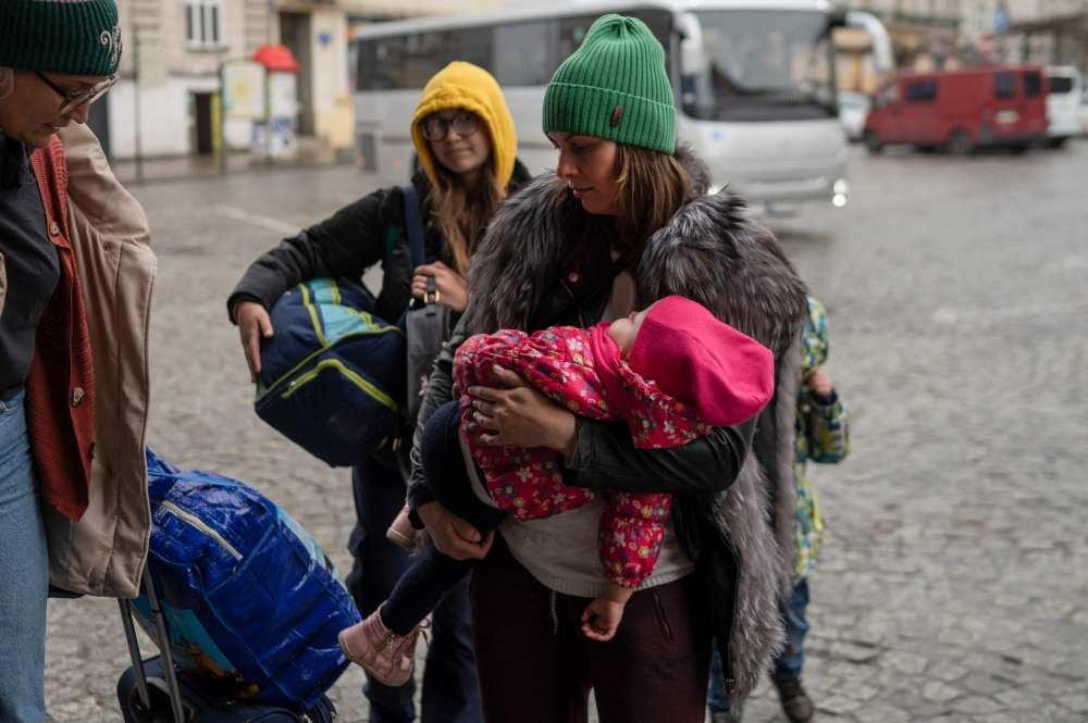 A woman carrying a baby arrives with other refugees from Ukraine at the main railway station in Przemysl, southeastern Poland, near the Polish-Ukrainian border on March 31, 2022