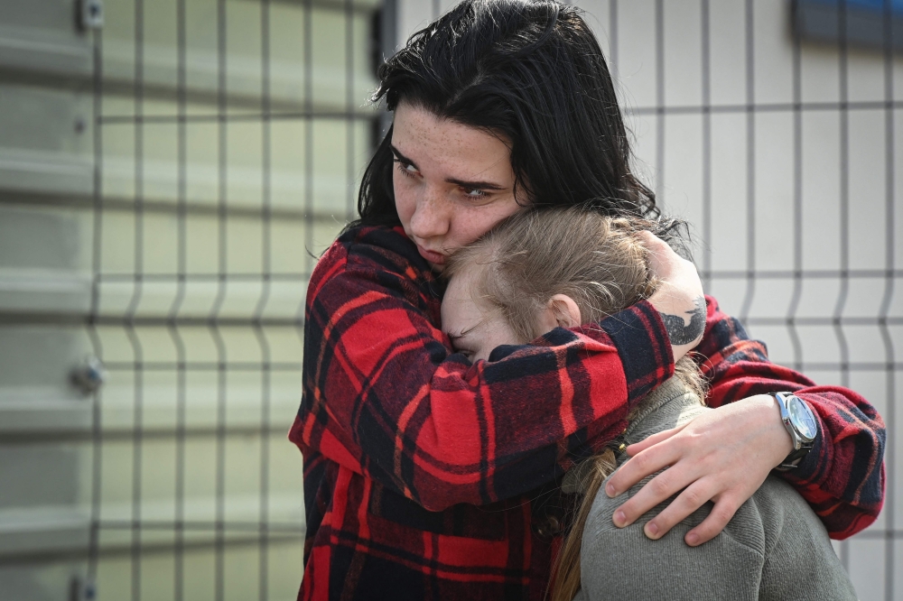 Ukrainian youth comfort each other as they wait to get on a bus at Palanca-Maiaky-Udobne border crossing point between Moldova and Ukraine. - AFP