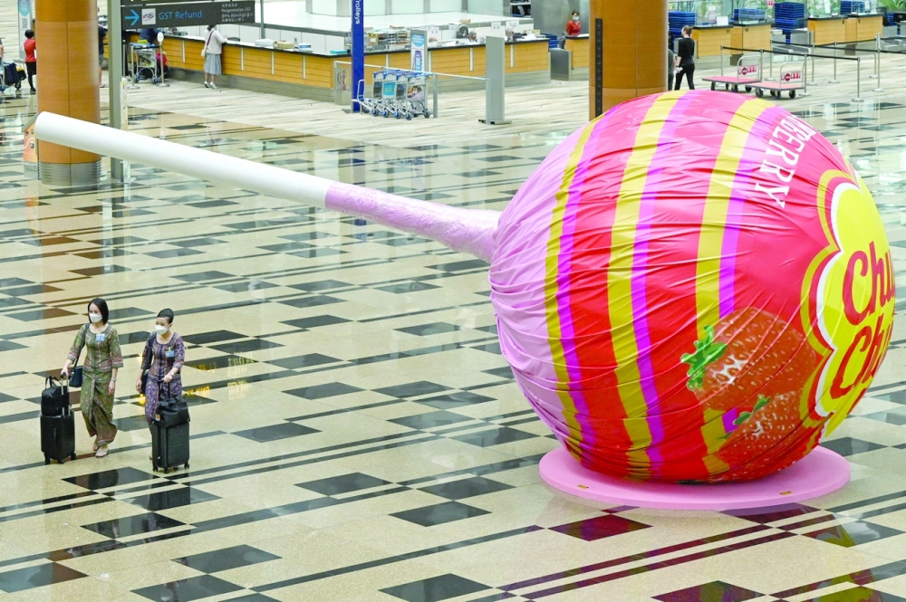 Stewardesses walk past a giant lollipop candy display at Changi International Airport in Singapore. -- AFP