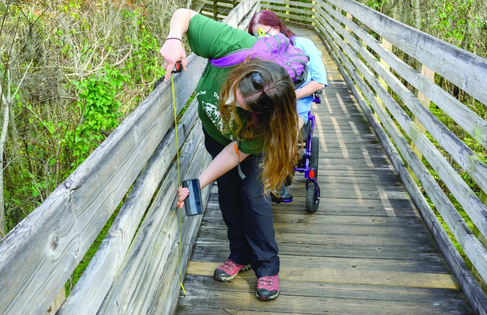 Syren Nagakyrie measures the height of the safety railing while on a hike with her mother, Vickie Boyer, at Lettuce Lake Conservation Park in Tampa on Dec. 3, 2021.  (Todd Anderson/The New York Times)