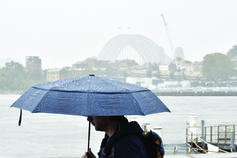 A man walks in front of the Harbour Bridge during rainfall in Sydney on Thursday, as inclement weather triggered evacuation orders in several suburbs of Sydney's south and southwest. - AFP
