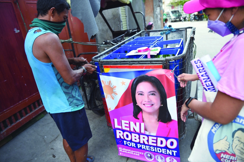 A volunteer for opposition presidential candidate and current vice-president, Leni Robredo, helping a delivery worker put a banner of Robredo on a tricycle during a house-to-house campaign in Las Pinas, suburban Manila. - AFP