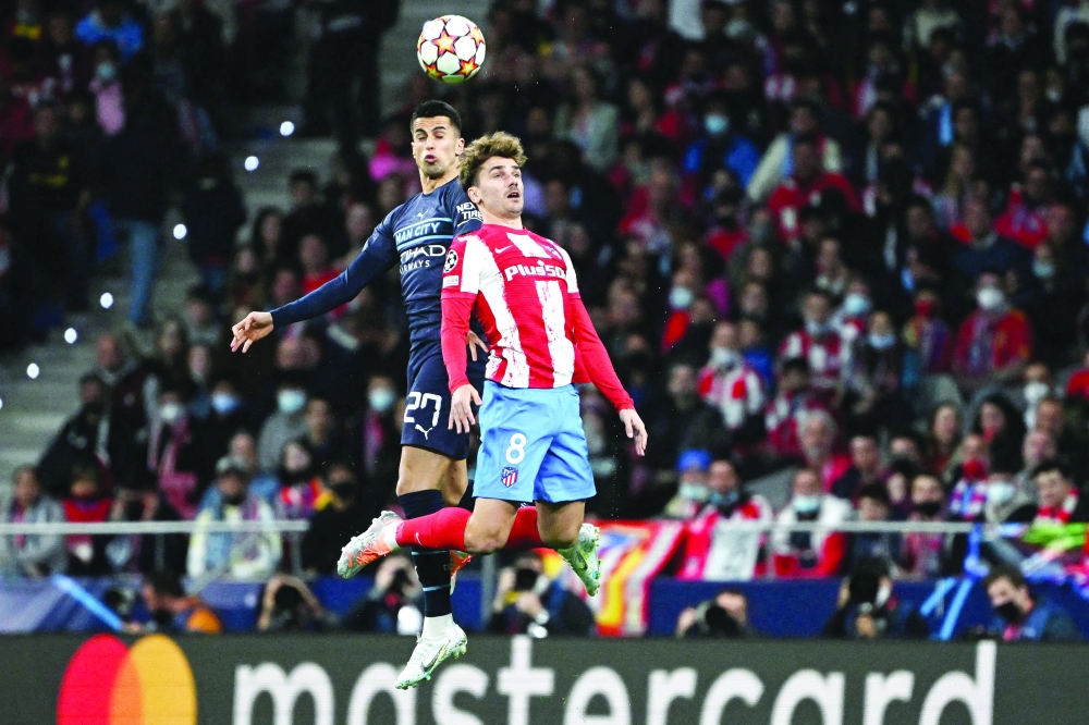 TOPSHOT - Manchester City's Portuguese defender Joao Cancelo (L) and Atletico Madrid's French forward Antoine Griezmann jump for a header during the UEFA Champions League quarterfinal second leg football match between Club Atletico de Madrid and Manchester City FC at the Wanda Metropolitano stadium in Madrid on April 13, 2022.  (Photo by Pierre-Philippe MARCOU / AFP)