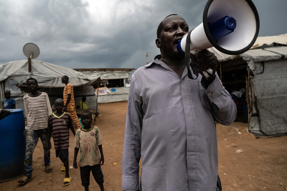 A worker with the South Sudan Ministry of Health calls for people in the Mangateen camp for internally displaced people to get their COVID-19 vaccines in Juba, South Sudan, on Oct. 19, 2021. (Lynsey Addario/The New York Times)