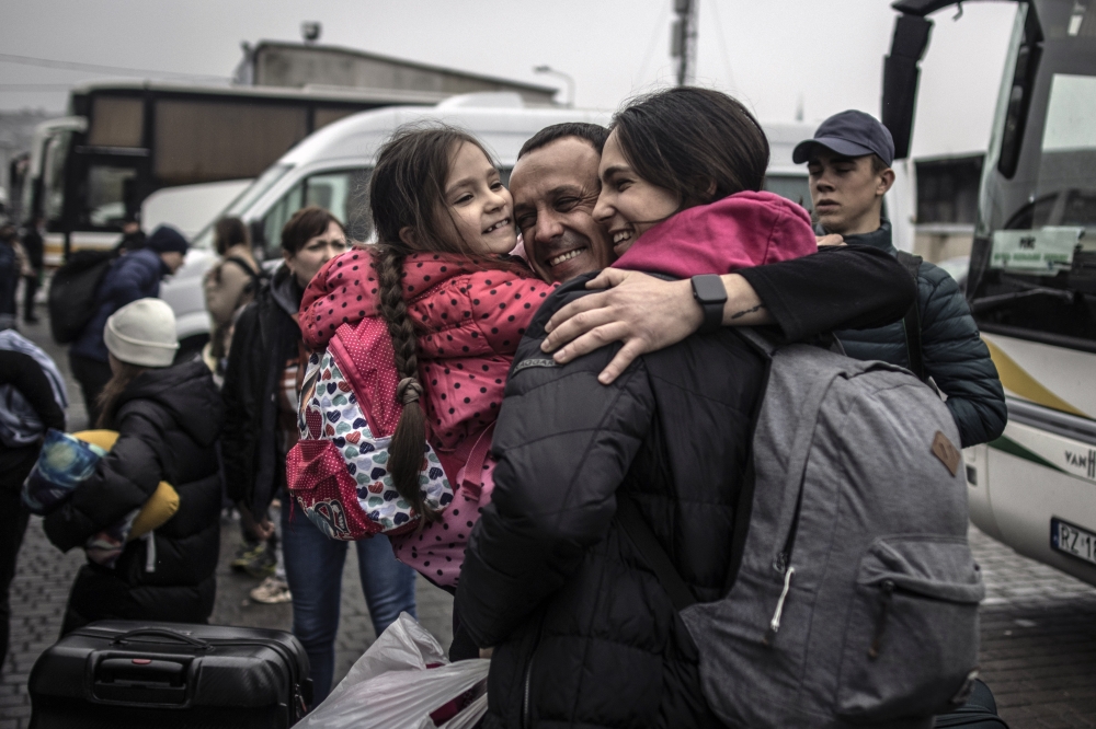 Pavlo, 38, embraces his daughter Eva, 6, and wife Marianna, 37, at the bus station in Lviv as we welcomes them back to Ukraine from Poland on Friday, April 22, 2022.  (Finbarr O'Reilly/The New York Times)