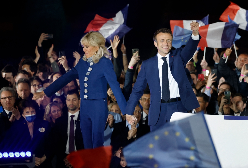 French President and La Republique en Marche (LREM) party candidate for re-election Emmanuel Macron (R) holds his fist in the air as he holds Brigitte Macron's hand after his victory in France's presidential election, at the Champ de Mars in Paris, on April 24, 2022.