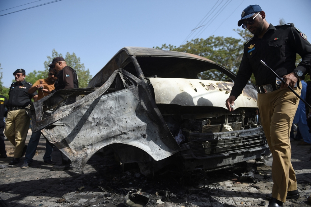 Police inspect a site around damaged vehicles following a bombing near the Confucius Institute affiliated with the Karachi University in Karachi. - AFP