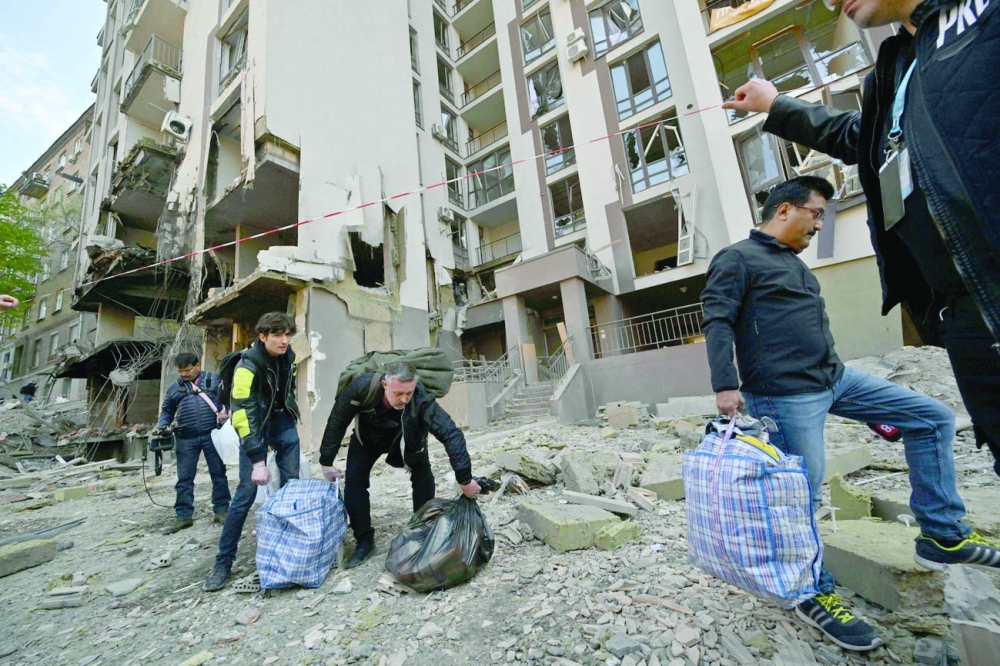 Residents carry their belongings as they leave their damaged building following Russian strikes in Kyiv on Friday amid Russian invasion of Ukraine. - AFP