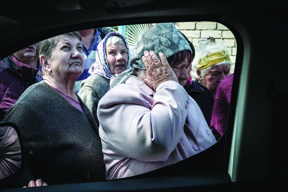 A woman covers her ears from the sound of mortar fire as people queue to collect pensions from a postal delivery van that reached the frontline despite the ongoing conflict in Mayaky, eastern Ukraine, on Friday. - AFP

