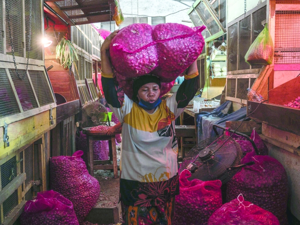 A vendor carries sacks of onion at a traditional market in Surabaya, Indonesia. — AFP