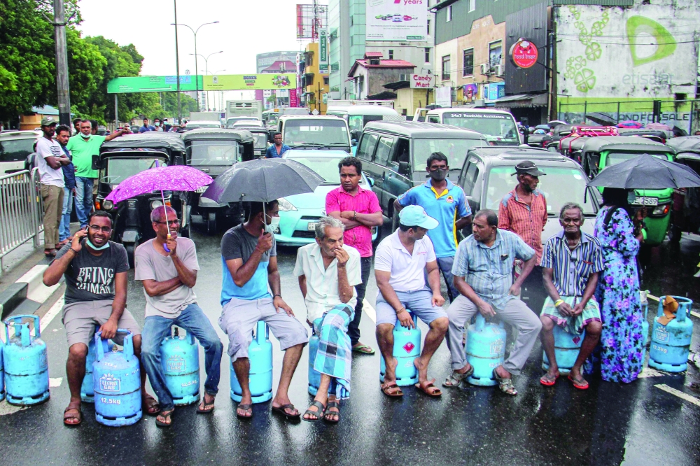 People sit on empty Liquefied Gas Cylinders (LPG) as they block a road to protest against shortage of fuel and cooking gas in Colombo on Friday. - AFP 