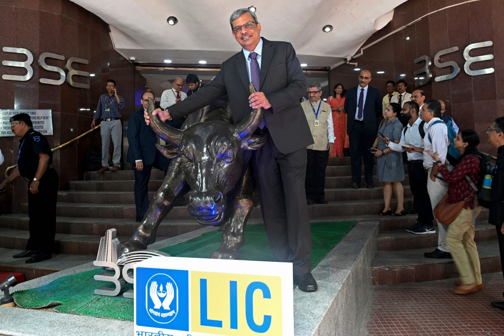 Mangalam Ramasubramanian Kumar (C), chairman of the Life Insurance Corporation of India (LIC) poses with the bronze statue of a bull at the Bombay Stock Exchange (BSE) in Mumbai on May 17
