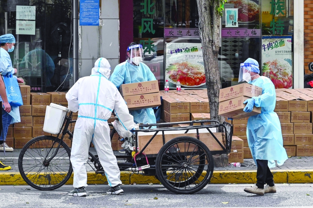 Workers wearing protective gear stack up boxes over a cart to deliver in a neighbourhood during a coronavirus lockdown in Shanghai. - AFP

