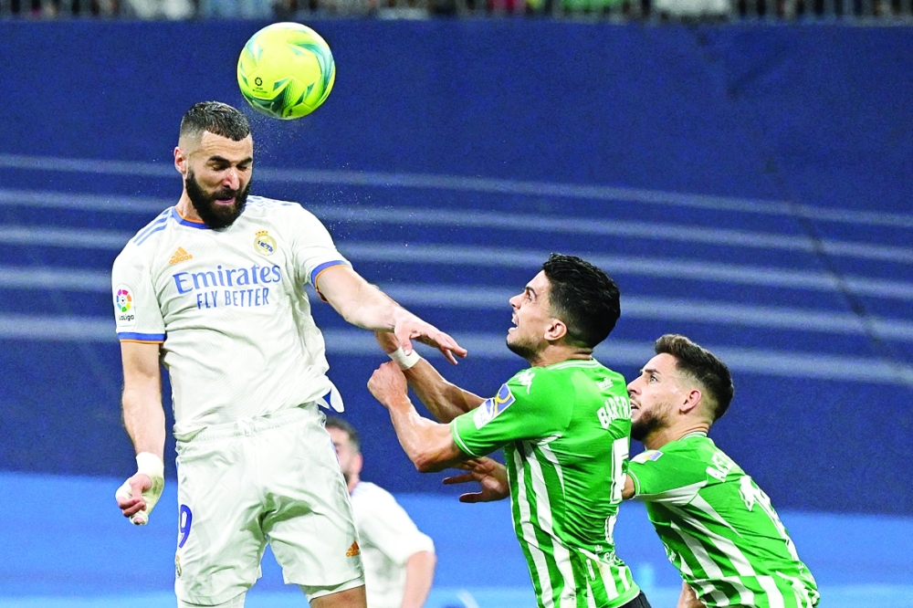 Real Madrid's French forward Karim Benzema (L) heads the ball next to Real Betis' Spanish defender Marc Bartra (C) and Real Betis' Spanish defender Alex Moreno during the Spanish league football match between Real Madrid CF and Real Betis at the Santiago Bernabeu stadium in Madrid on May 20, 2022. (Photo by Pierre-Philippe MARCOU / AFP)

