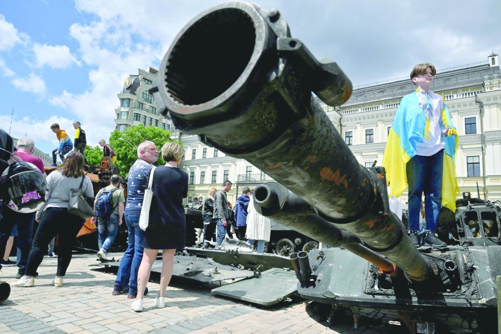A boy with the Ukrainian flag draped across his shoulders, stands on the turret of a tank during the opening of the exhibition of destroyed Russian military equipment in the centre of Ukrainian capital of Kyiv on Saturday. - AFP