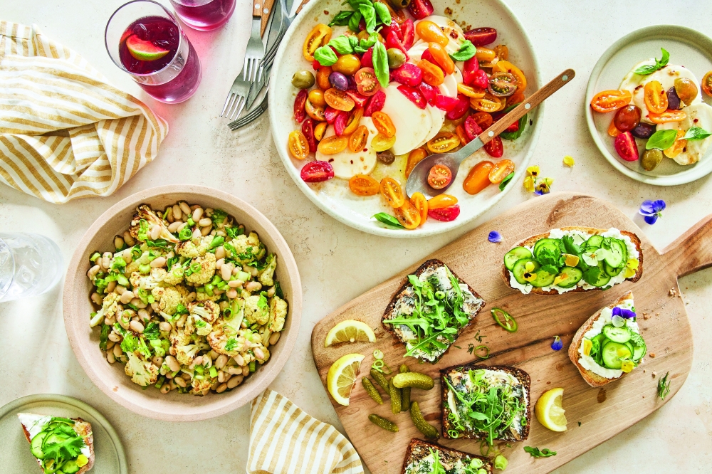A picnic spread, Clockwise from bottom left: a white bean salad with roasted cauliflower; Caprese-style marinated mozzarella with cherry tomatoes and olives; open-faced cucumber-ricotta sandwiches; and sardines on buttered brown bread. (Kate Sears/The New