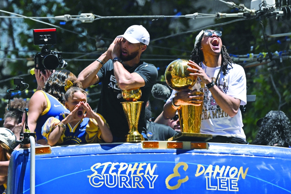 US basketball player Stephen Curry (L) holds the MVP trophy alongside team-mate Damion Lee (R) as they celebrate from a double decker bus during the Golden State Warriors NBA Championship victory parade in San Francisco. -- AFP