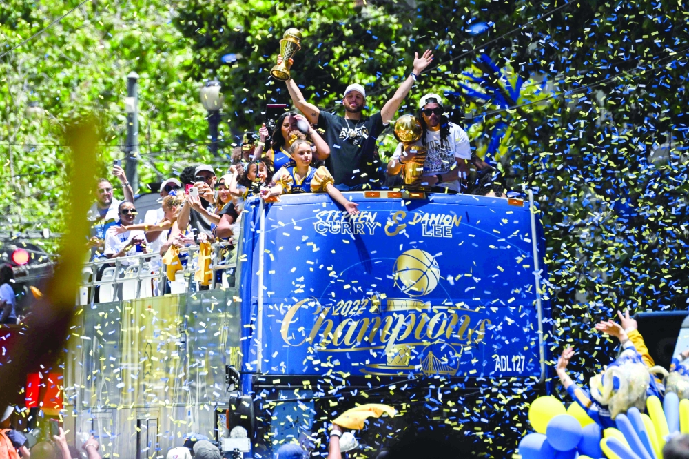 Stephen Curry and Damion Lee hold trophies as they wave from a confetti-covered double-decker bus. -- AFP