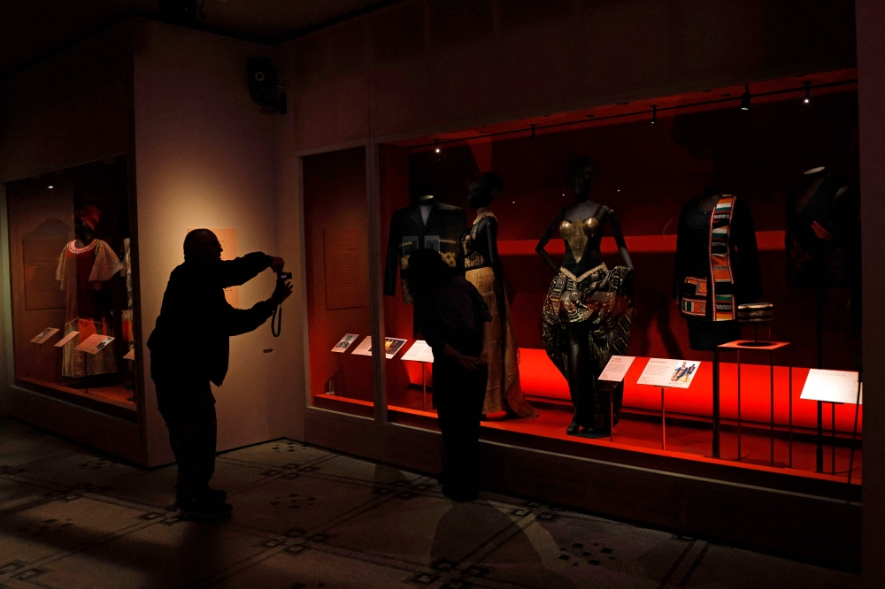 A man takes a picture of the dress know as "Tuareg Artistry" designed by Alphadi, during a photo call for the 'Africa Fashion' exhibition at the Victoria and Albert museum in London on June, 27, 2022.  Over 250 objects are on display for the exhibition, with approximately half of these drawn from the museum痴 collection, including 70 new acquisitions. Many of the garments on show are from the personal archives of a selection of iconic mid-twentieth century African designers. (Photo by CARLOS JASSO / AFP)


