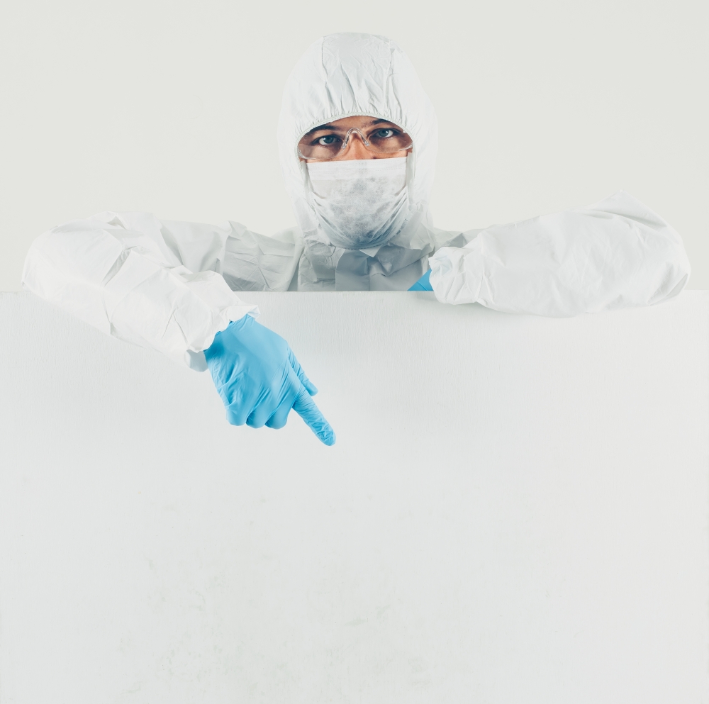 A doctor in mask, gloves and protective suit pointing down in white background . space for text. coronavirus