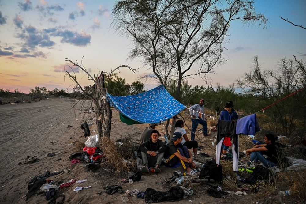 Migrants rest after crossing the Rio Grande River as they wait to get apprehended by Border Patrol agents in Eagle Pass, Texas, at the border with Mexico on Thursday. - AFP 