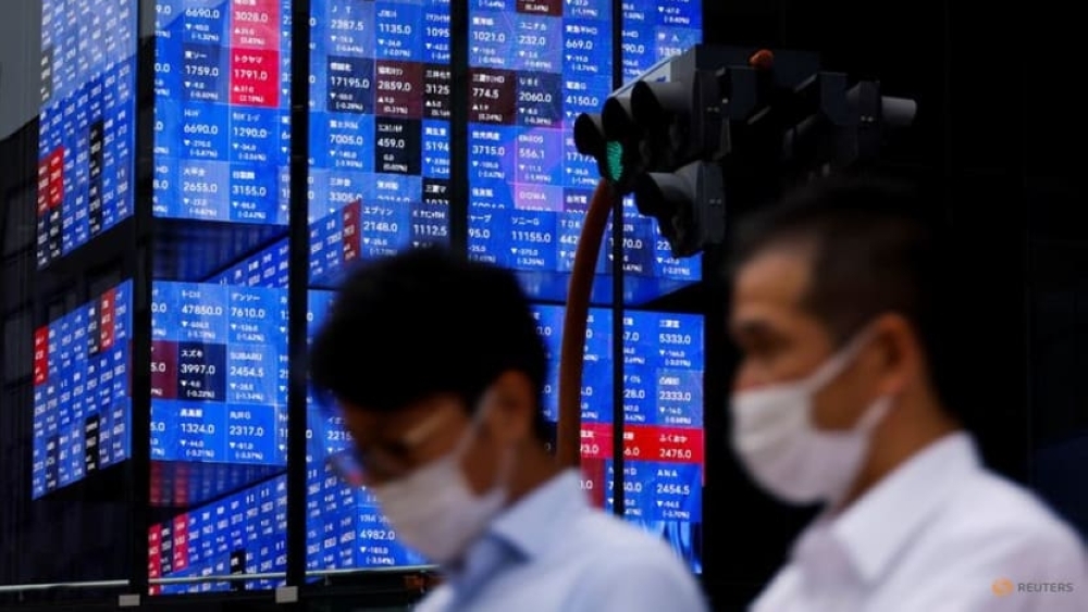 People pass by an electronic screen showing Japan's Nikkei share price index inside a conference hall in Tokyo.  - Reuters File